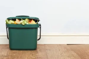 Green waste bin filled with food waste in a minimalistic room.